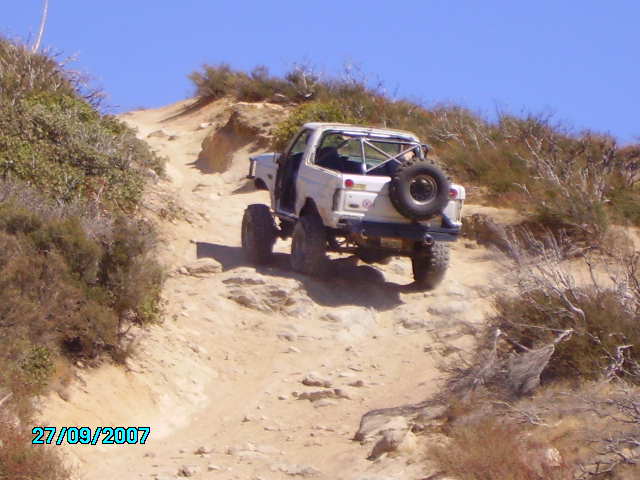 White off-road SUV with spare tire on rear climbing a steep dirt hill