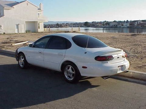 1999 Ford Taurus - Rear view of a white 1999 Ford Taurus sedan parked on a street next to a body of water.
