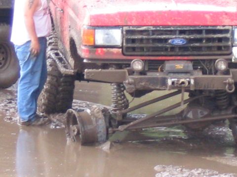 1989 Ford Bronco - A red 1989 Ford Bronco is stuck in mud, its front wheel having detached from the axle.