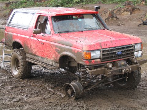 1989 Ford Bronco - Muddy red 1989 Ford Bronco with a detached front wheel, stuck off-road.