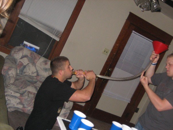 Two men are using a funnel and tube to pour liquid into a cup