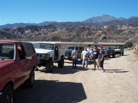 1995 Ford Bronco - A group of people stand near their off-road vehicles on a sunny day with mountains in the distance.