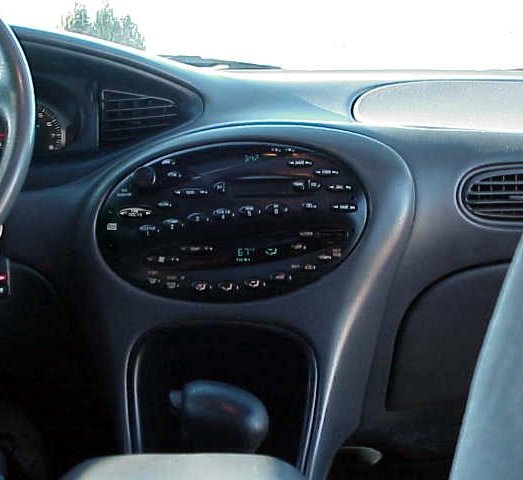Car interior dashboard with oval-shaped center console, radio, and gear shifter. Gray dashboard and black accents