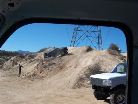 1995 Ford Bronco - Two Ford Broncos navigate a sandy off-road course under a clear blue sky with a power line tower overhead.