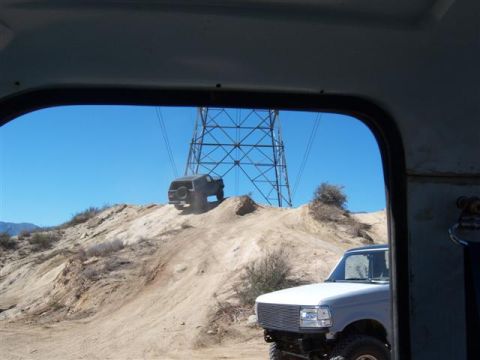 1995 Ford Bronco - Two SUVs navigate a sandy incline under a large power line tower on a clear day.