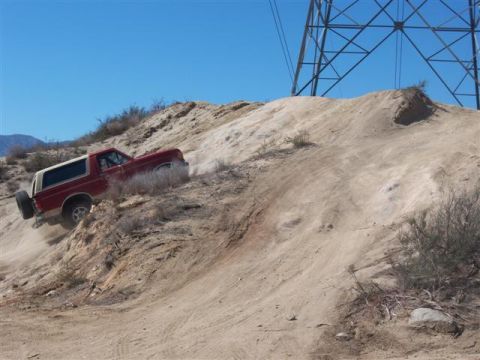 1995 Ford Bronco - 1995 Ford Bronco navigating a challenging off-road trail under a clear blue sky.