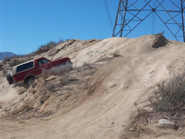 Red 1995 Ford Bronco climbing a steep dirt hill with a power line tower in the background