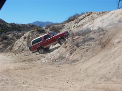 1995 Ford Bronco - A red Ford Bronco navigates a challenging off-road trail on a sunny day.