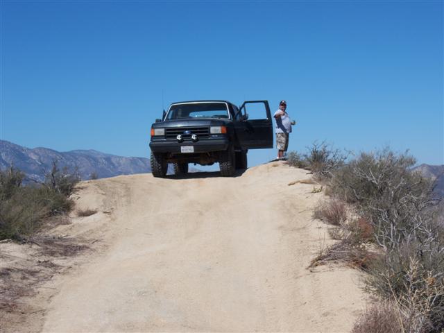Dark gray Ford Bronco parked on a dirt road with its driver's door open
