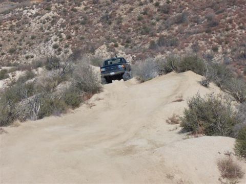 1995 Ford Bronco - A dark SUV navigates a steep, sandy incline in a dry, brushy landscape.