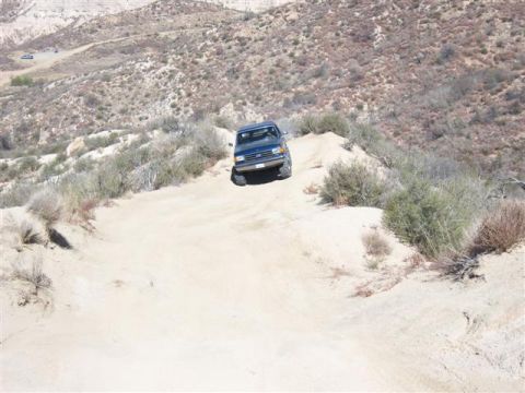 1995 Ford Bronco - A blue 1995 Ford Bronco navigates a steep dirt trail in a dry, hilly landscape.
