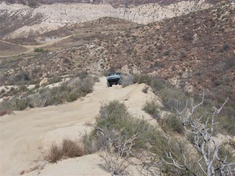 1995 Ford Bronco - A dark SUV navigates a dusty trail through a barren, mountainous terrain.