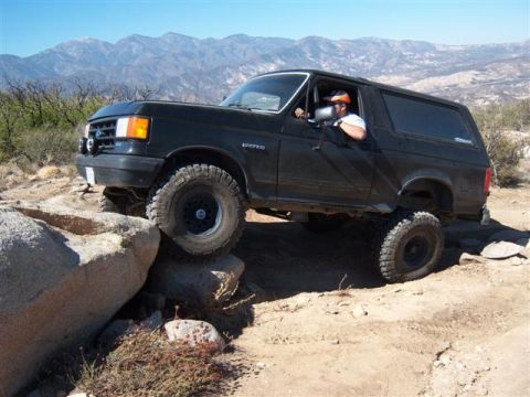 1995 Ford Bronco - A driver navigates a black Ford Bronco over large rocks on a off-road trail.