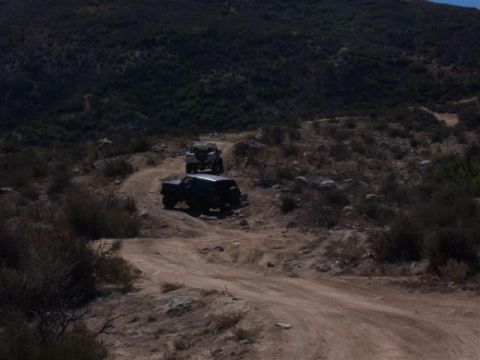 1995 Ford Bronco - Two SUVs navigate a challenging dirt path through a dry, hilly landscape.