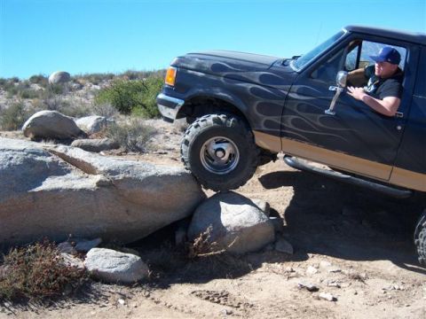 1995 Ford Bronco - A 1995 Ford Bronco navigates a challenging rocky off-road course under a clear blue sky.
