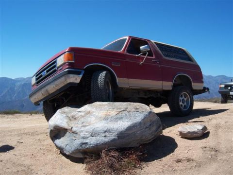 1995 Ford Bronco - A red Ford Bronco is positioned on a large rock with a second vehicle visible in the distance.