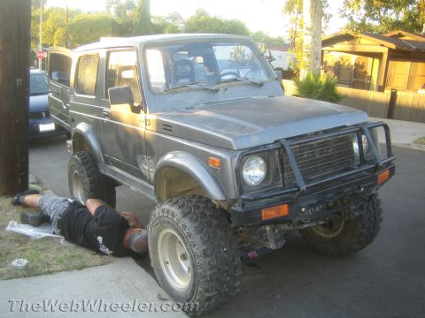 1987 Suzuki Samurai - A person works on a Suzuki Samurai parked on a residential street.