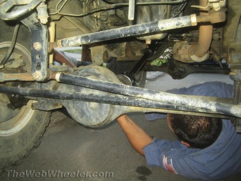 1987 Suzuki Samurai - Mechanic works on the rear axle of a 1987 Suzuki Samurai, focusing on the suspension and drivetrain components.