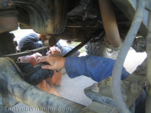 1987 Suzuki Samurai - Mechanics work on the underside of a vehicle, focusing on suspension and exhaust components.