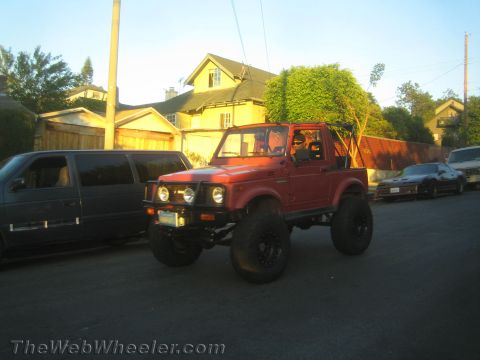 1987 Suzuki Samurai - A red, lifted off-road vehicle is parked on a residential street with other vehicles present.