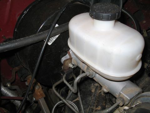 1989 Ford Bronco - Close-up of a brake master cylinder and booster assembly, showing the white plastic fluid reservoir.