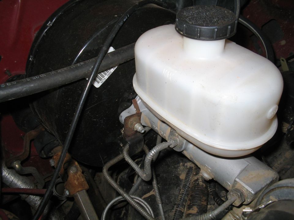 Brake master cylinder and booster assembly with white plastic reservoir. Label visible on black hose