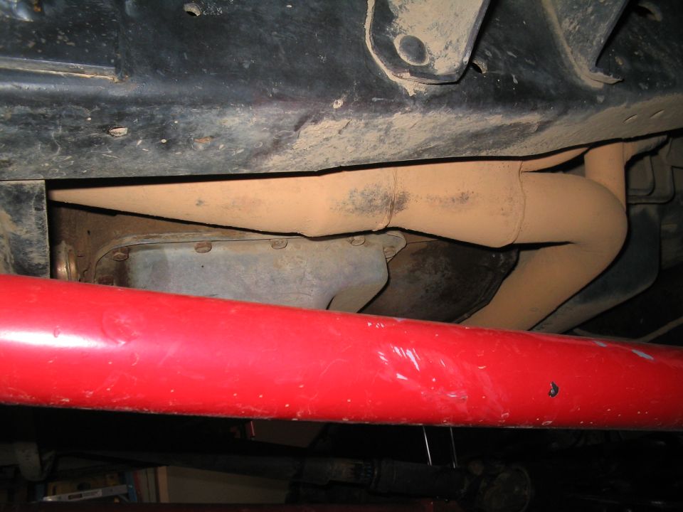 Underside of a vehicle showing rusty exhaust pipes and a red bar