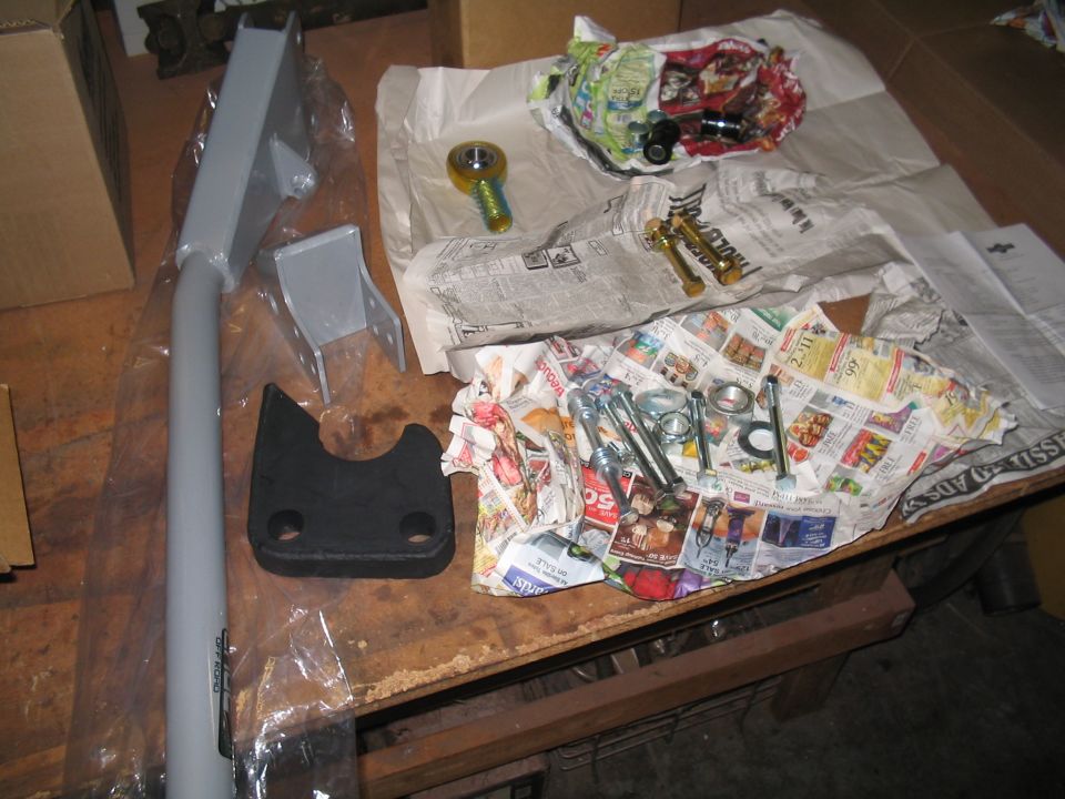 Gray tubular suspension link, mounting brackets, heim joint and bolts laid out on a workbench