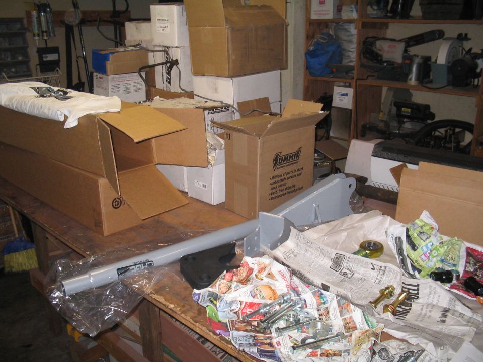 Garage workbench with Summit Racing boxes, a gray suspension link and loose hardware