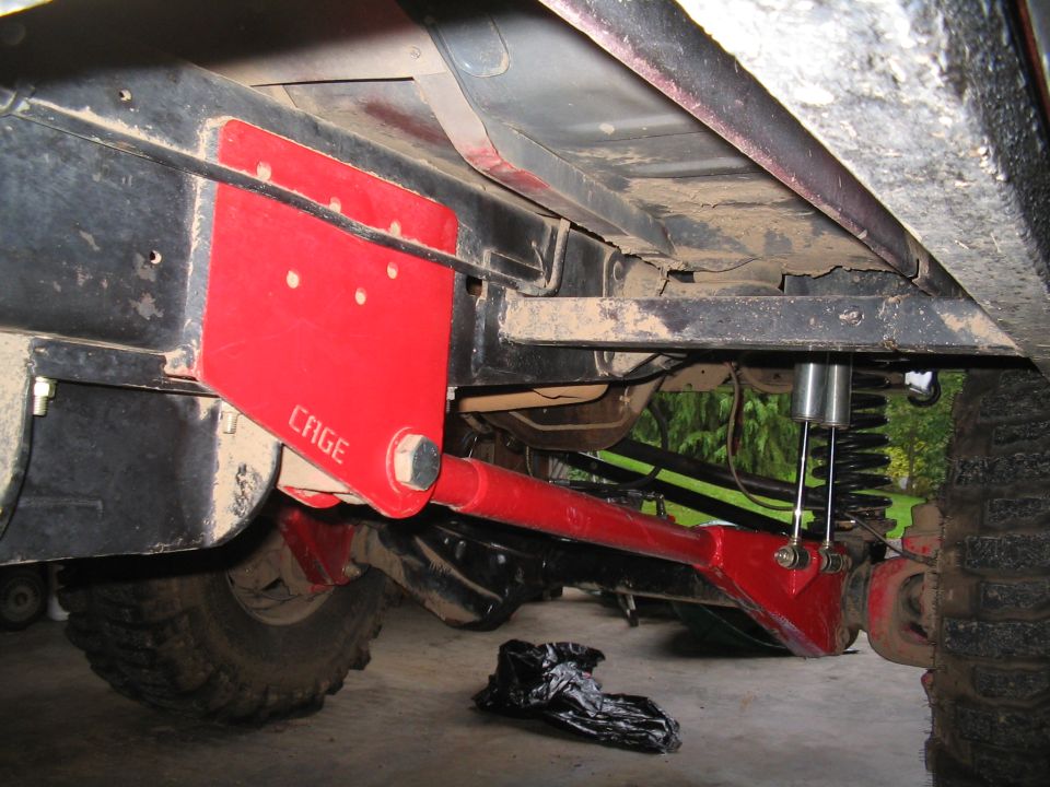 Red CAGE radius arm and coil spring suspension under a lifted truck in a garage