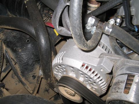 1989 Ford Bronco - Close-up view of an alternator with associated hoses and belts within an engine compartment.