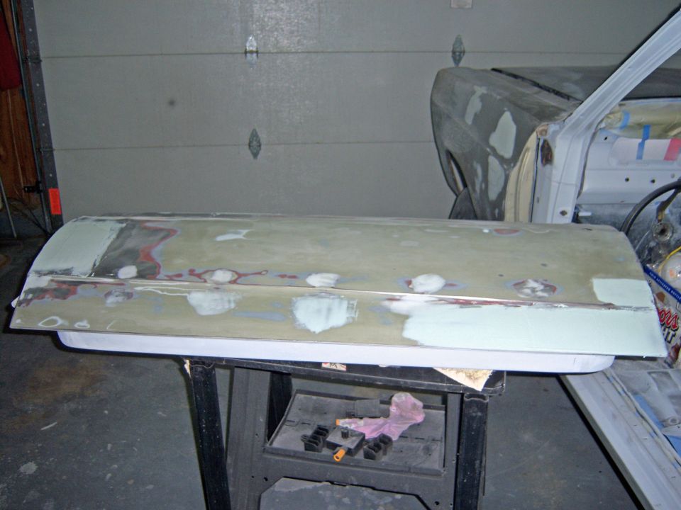 1967 Ford Ranchero door with body filler and primer, resting on a stand