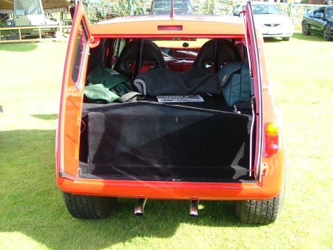 1988 Ford Sport - The rear of an orange hatchback is shown with its hatch open, revealing racing seats and a large subwoofer box.