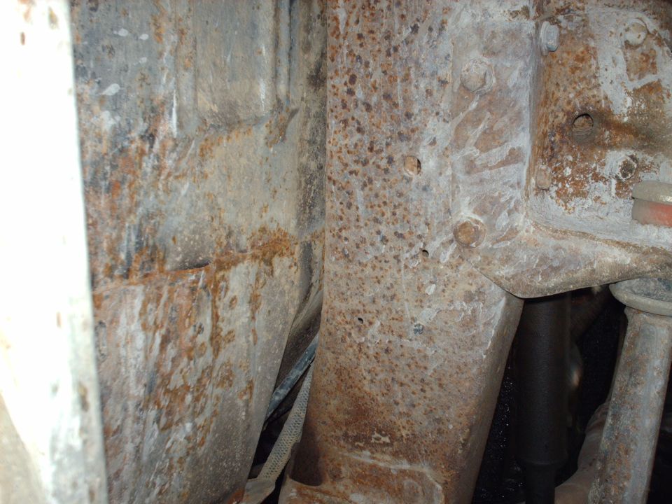 Close-up of heavily rusted metal frame and suspension parts, showing corrosion and some visible bolts