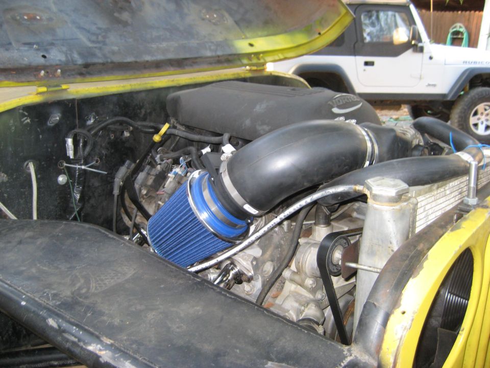 Jeep engine bay with blue air filter and Vortec intake. Another Jeep is parked behind it