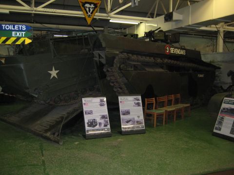 1966 Jeep CJ5 - An amphibious landing craft, marked "3 SEVENOAKS", is displayed indoors with informational signs and chairs nearby.