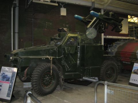 1966 Jeep CJ5 - An armored vehicle with a missile launcher is displayed indoors, with another camouflaged vehicle nearby.