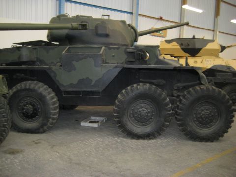 1966 Jeep CJ5 - An armored car with a camouflage paint scheme is visible in an indoor setting, with another military vehicle behind it.