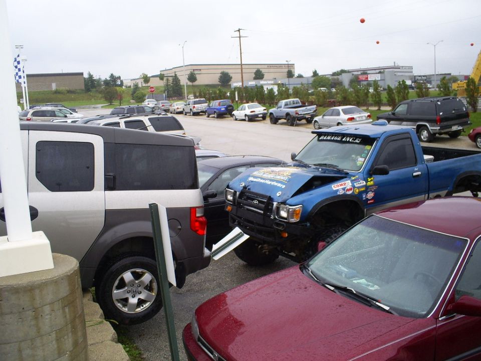 Blue pickup truck with a dented hood and stickers parked in a lot