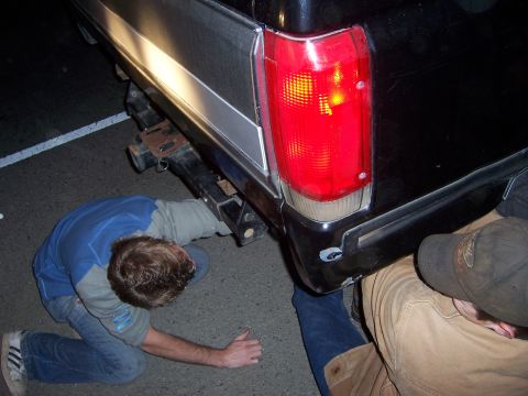 1991 Ford Bronco - Two people examine the rear of a black 1991 Ford Bronco, focusing on the bumper and taillight assembly.