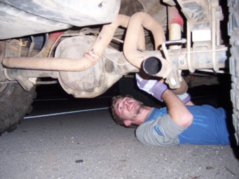 1991 Ford Bronco - A person works on the underside of a vehicle, focusing on the exhaust pipe and rear axle.