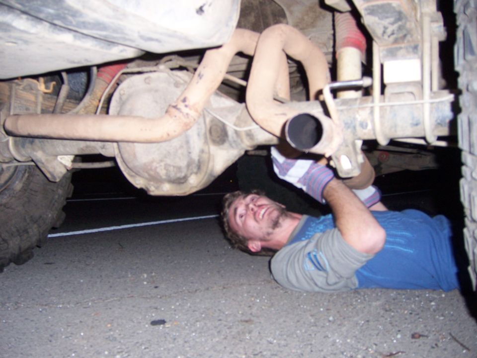 Man lying on the ground working on the exhaust system of a vehicle