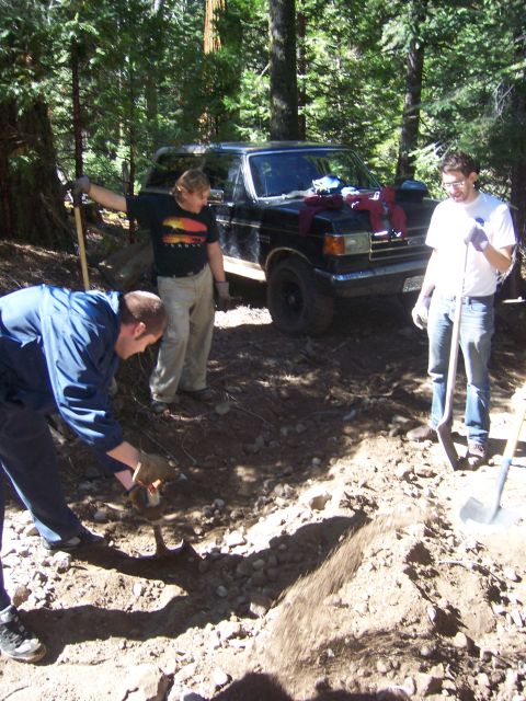 1991 Ford Bronco - A black 1991 Ford Bronco is visible in the background as people work on a dirt path in a wooded area.