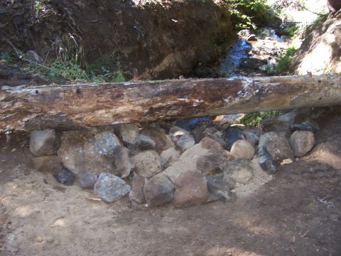 1991 Ford Bronco - A natural scene depicts a fallen log resting on a collection of rocks, with a small stream flowing in the background.