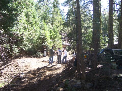 1991 Ford Bronco - A group of people stand near a dark SUV parked on a dirt path in a wooded area.