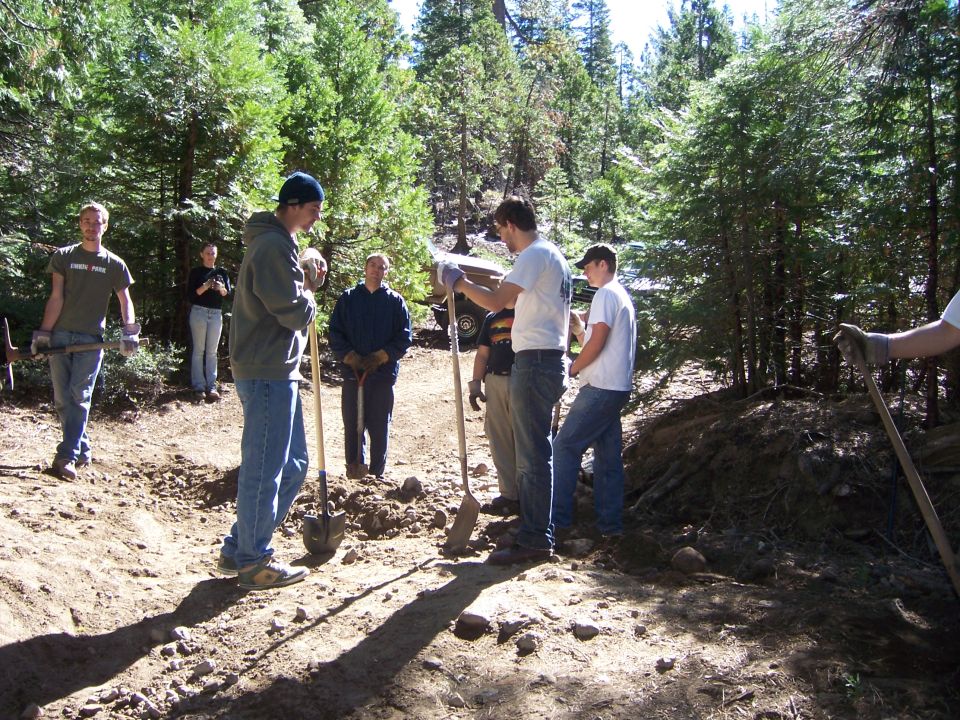 People with shovels and pickaxes working on a dirt path in a wooded area