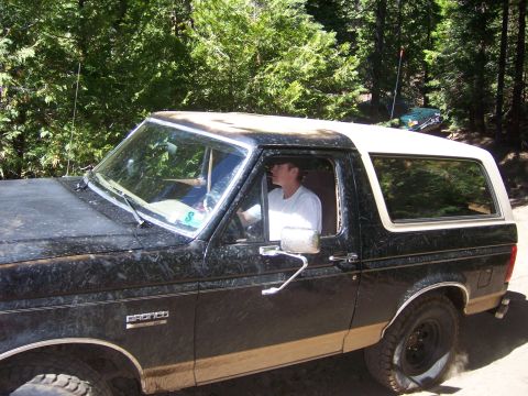 1991 Ford Bronco - A driver is visible inside the dusty black and tan Ford Bronco with a white removable top.