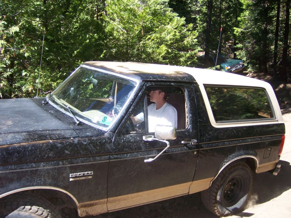 Black and tan Ford Bronco with a white top, seen from the side at a 3/4 front angle
