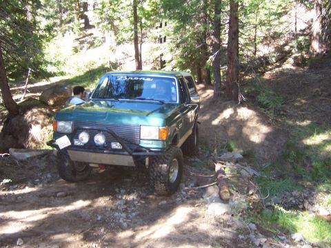 1991 Ford Bronco - 1991 Ford Bronco navigating a wooded trail with rocky terrain.