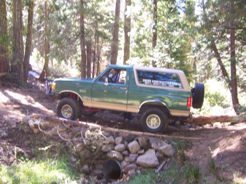 1991 Ford Bronco - A green 1992 Ford Bronco navigates a wooded trail, crossing over a fallen log.